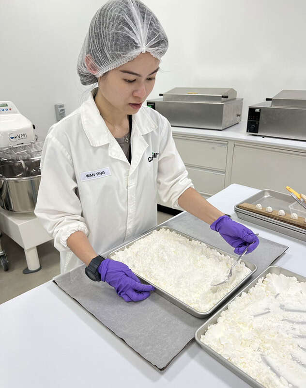 一位穿着白色实验服的妇女站在食品科学实验室里低头看。